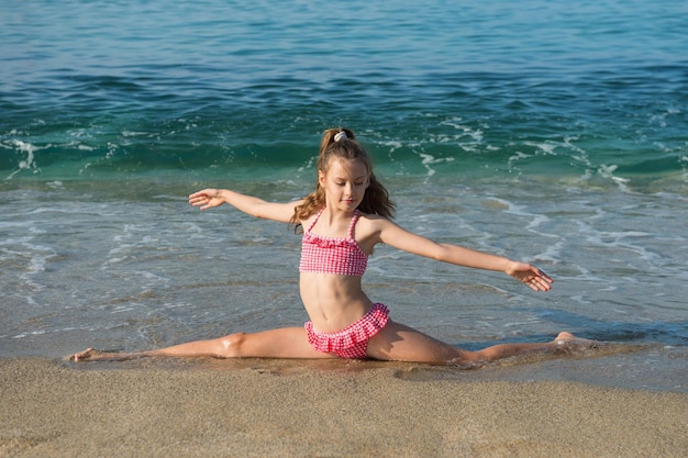 Beautiful sporty girl in red swimming suit is doing the splits on the beach