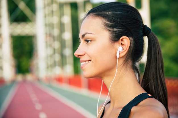 Beautiful sporty slim brunette woman in sportswear and headphones on morning exercises outdoors