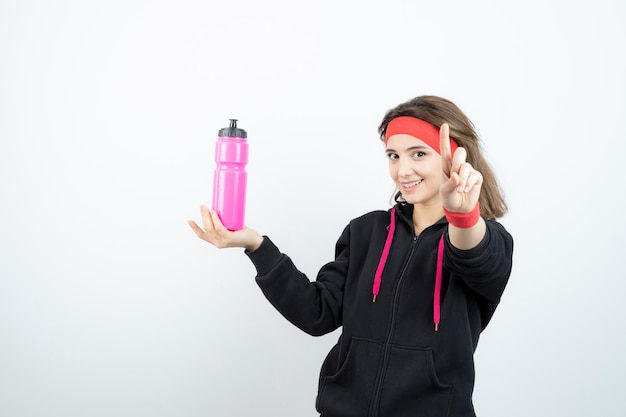 Beautiful sporty woman holding bottle with water and pointing up .