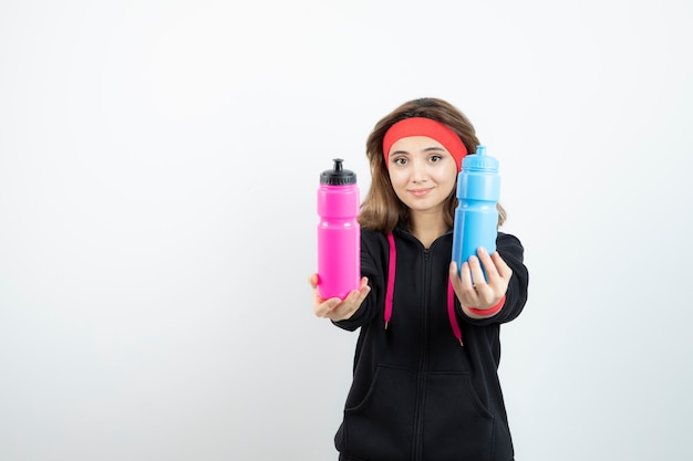 Beautiful sporty woman holding bottles with water on white wall .