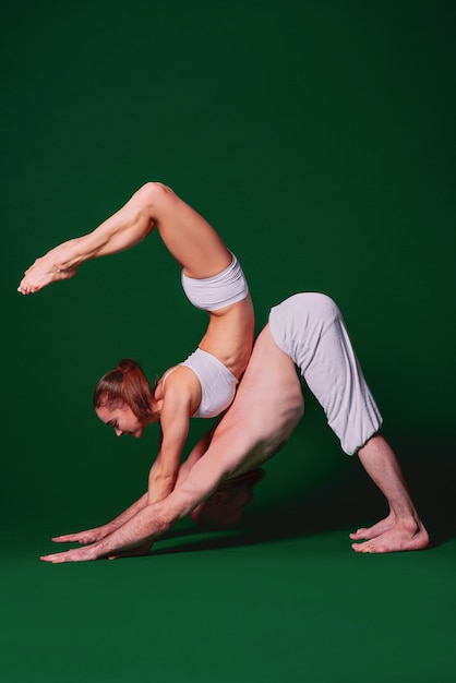 Beautiful sporty woman and man in white clothes doing yoga asanas together indoor