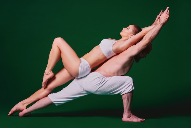 Beautiful sporty woman and man in white clothes doing yoga asanas together indoor