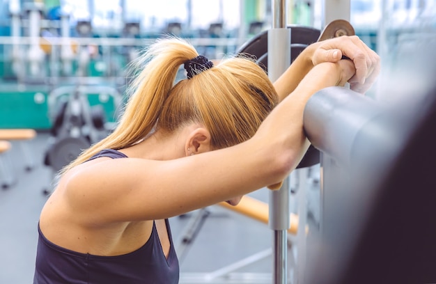 Beautiful sporty woman resting tired after lifting barbell on a muscular training in fitness center