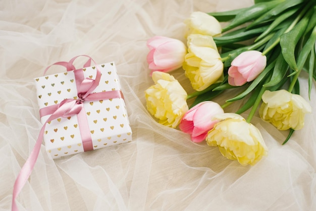 Beautiful spring bouquet of pink and yellow tulips and a gift with a ribbon on a beige background