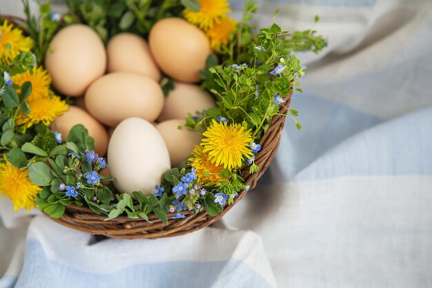 Красивый весенний букет в деревянной корзине с пасхальными крашеными яйцами, яйцами с милыми лицами. Пасхальная красочная открытка. Вид сверху.