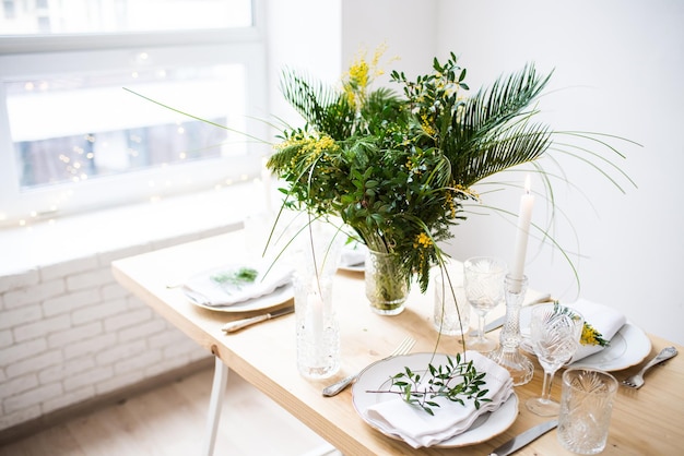 Beautiful springtime table setting with green leaves and mimosa branches