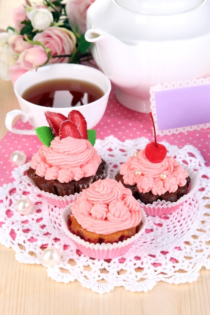 Beautiful strawberry cupcakes and flavored tea on dining table close-up