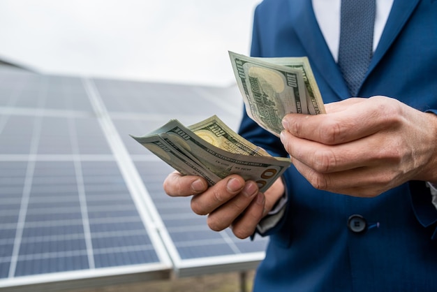 Beautiful strong hands holding a round sum of bank new dollars on a background of new solar panels Green electricity concept