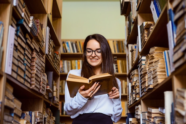 本でいっぱいの棚の間の図書館に美しい学生が立っている