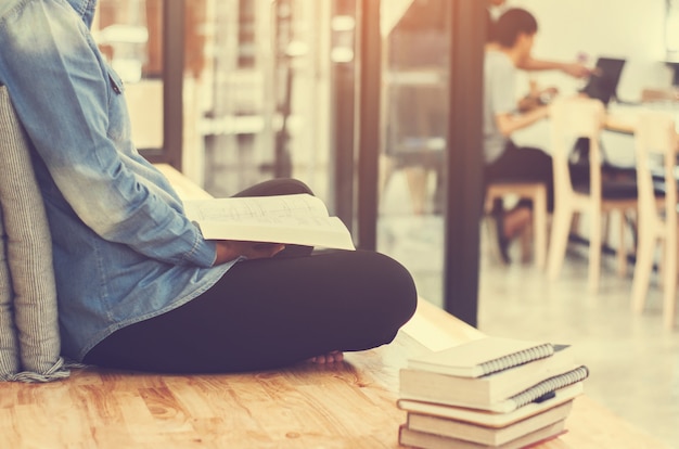 Beautiful student woman sitting at the stair and reading a book with blurred cafe workplace