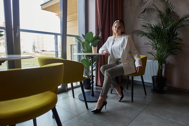 beautiful and stylish blonde woman, dressed in stylish clothes, sits in a trendy cafe