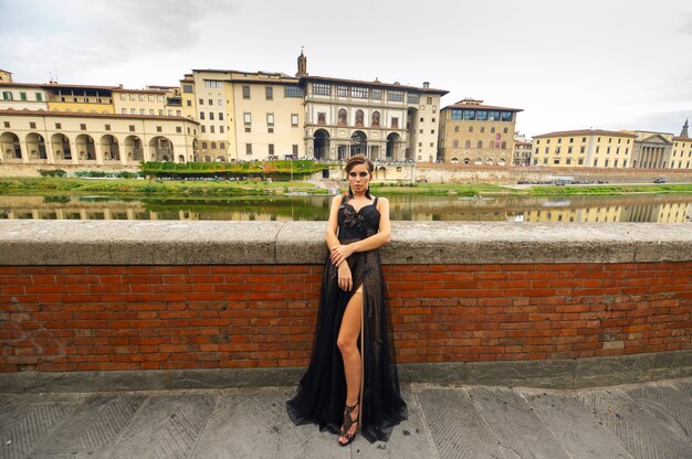 Beautiful stylish bride in a black dress stands on the embankment in Florence, Italy