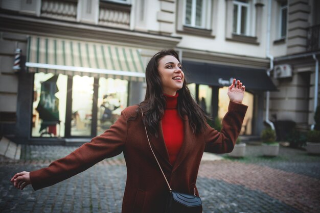 Foto una bella donna bruna elegante con i capelli lunghi in un cappotto rosso cammina per la strada la sera dopo lo shopping