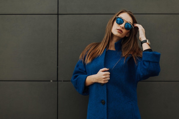 A beautiful stylish fashionable woman in a fur coat hat and glasses posing on the street