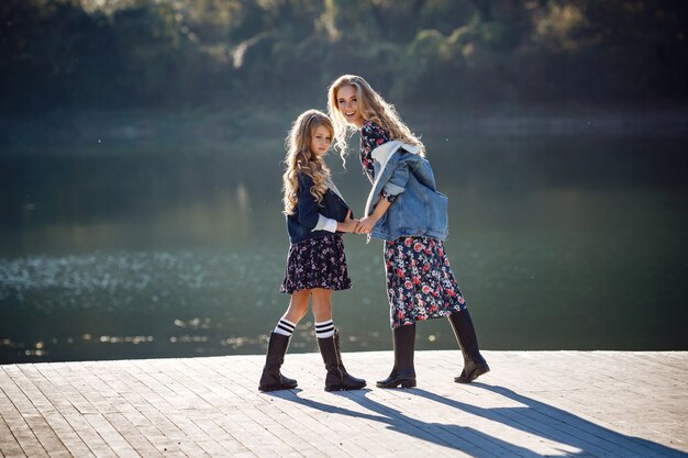 Beautiful stylish girl friends near a mountain lake in the forest, denim style. The idea and concept of a happy childhood, sisterhood and unity with nature