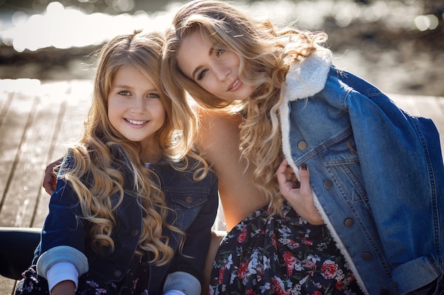 Beautiful stylish girl friends near a mountain lake in the forest, denim style. The idea and concept of a happy childhood, sisterhood and unity with nature