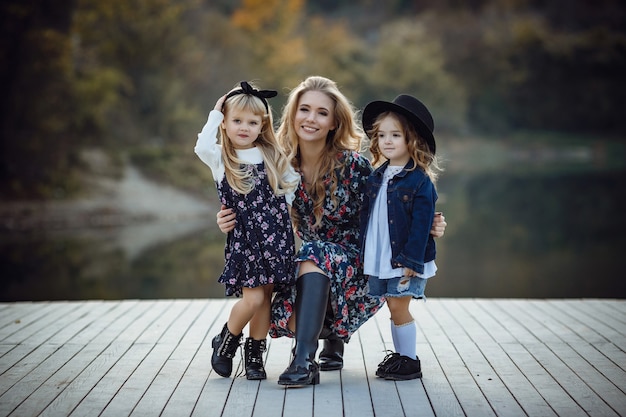 Beautiful stylish girl friends near a mountain lake in the forest, denim style. The idea and concept of a happy childhood, sisterhood and unity with nature