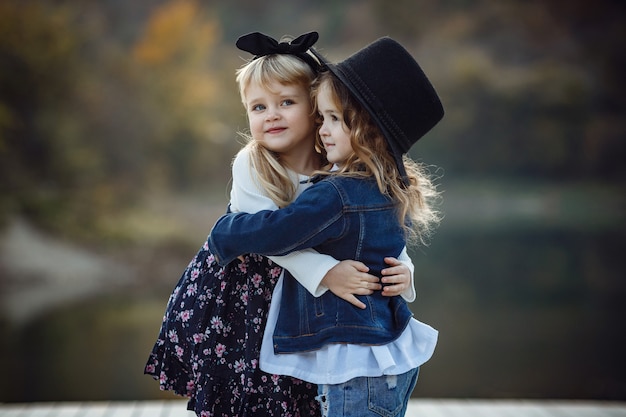 Beautiful stylish girl friends near a mountain lake in the forest, denim style. The idea and concept of a happy childhood, sisterhood and unity with nature