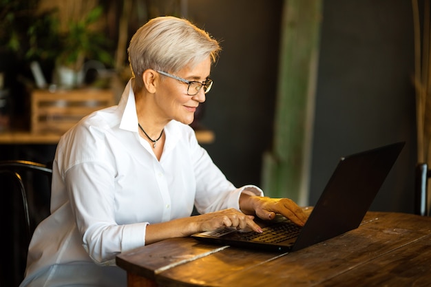 beautiful stylish woman aged in glasses at the table with a laptop