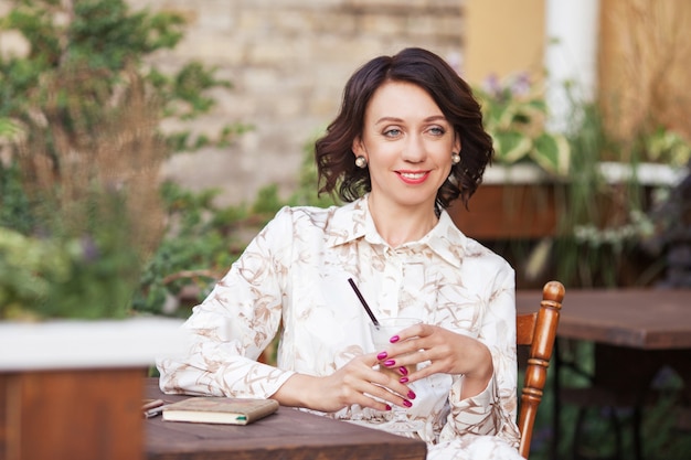 Beautiful stylish woman in beige dress drinking coffee outdoors at the cafe. Portrait of happy female in open air cafe