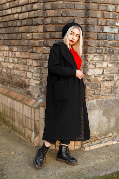 Beautiful stylish woman in a black coat with a red jersey in a black beret near a vintage brick wall