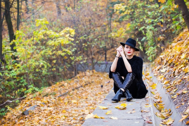 Beautiful stylish woman in a black hat in autumn park