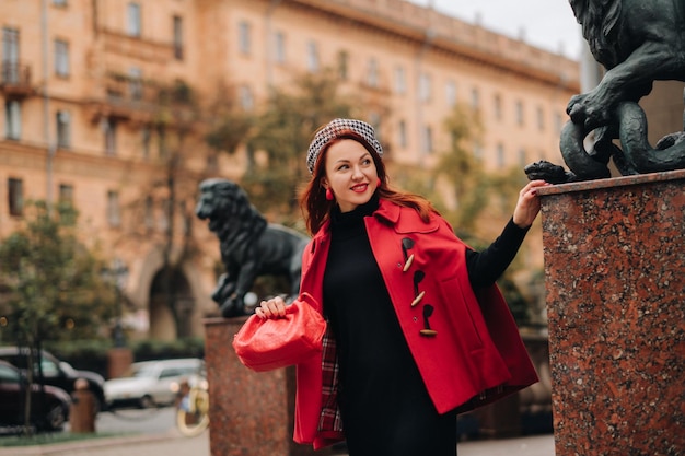 A beautiful stylish woman dressed in an elegant red coat with a stylish red handbag in the autumn city