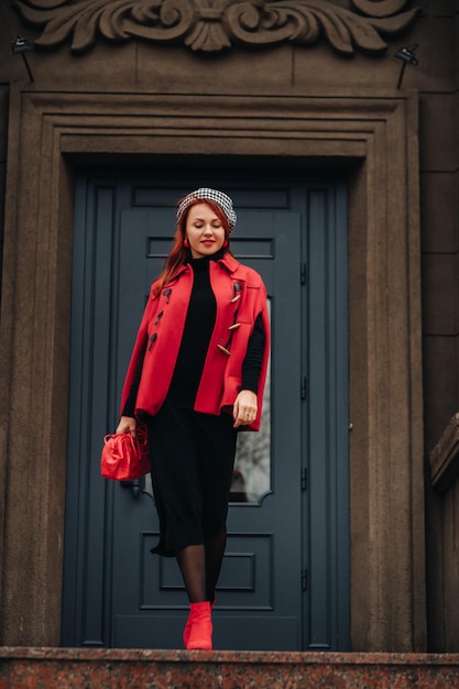 A beautiful stylish woman dressed in an elegant red coat with a stylish red handbag in the autumn city