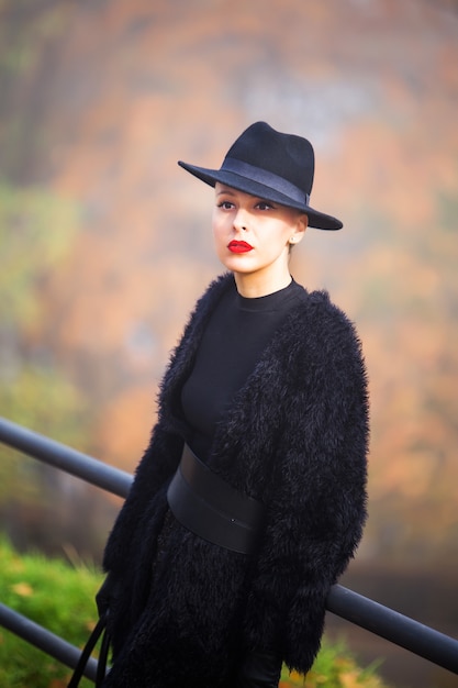 Фото Красивая стильная женщина в черной шляпе в осеннем парке