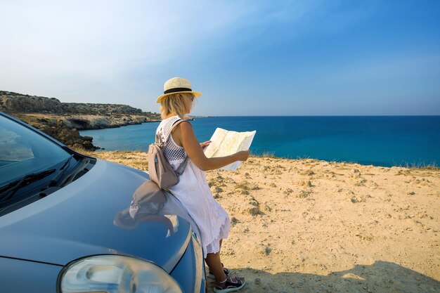 아름답고 세련된 여성이 차로 여행하고 있습니다. 성숙한 여성 여행자는 자동차로 여행하고 바다, 키프로스에 대한 로드맵을 봅니다.