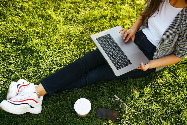 Beautiful stylish woman sitting on green grass with laptop