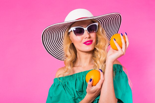 Bella donna alla moda in occhiali da sole e cappello con le arance