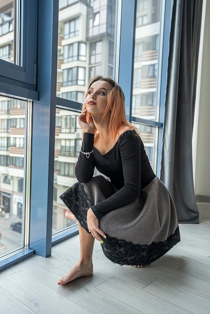 Beautiful stylish young girl with wellgroomed hair near the spacious windows The concept of a girl by the window