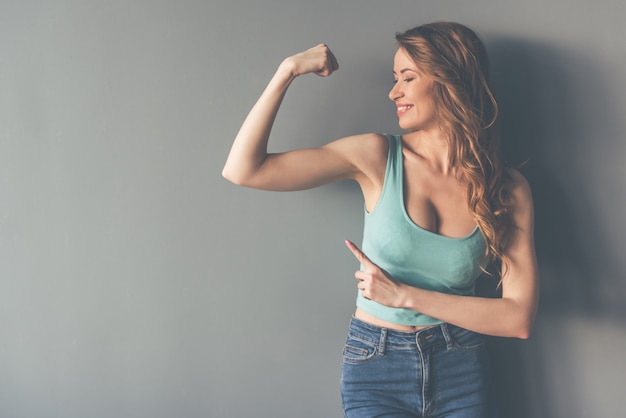 La bella giovane donna alla moda sta indicando sui suoi muscoli.