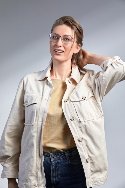 A beautiful stylishly dressed middleaged woman in stylish glasses smiles and poses at the camera a woman 3545 years old blonde with good healthy skin in glasses on a gray background