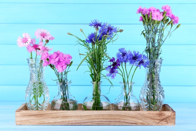 Beautiful summer flowers in vases on blue wooden background