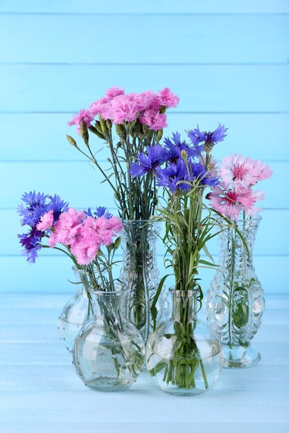 Красивые летние цветы в вазах на синем деревянном фоне