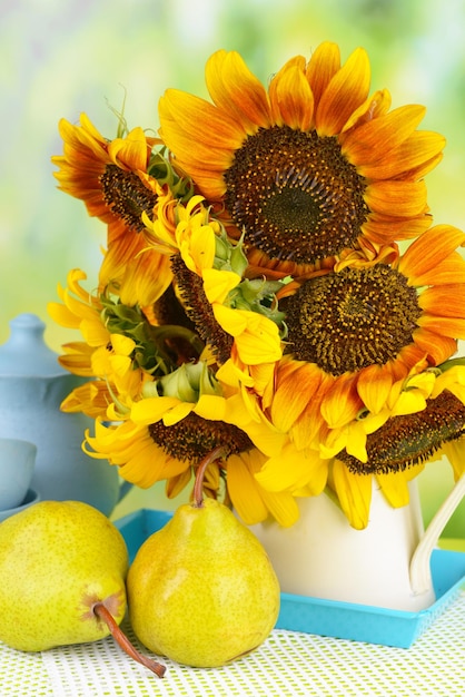 Beautiful sunflowers in pitcher with pears on table on bright background