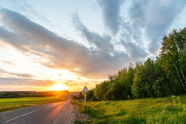 Beautiful sunset over an empty road in the countryside an empty\
asphalt road runs along a field and forest during sunset