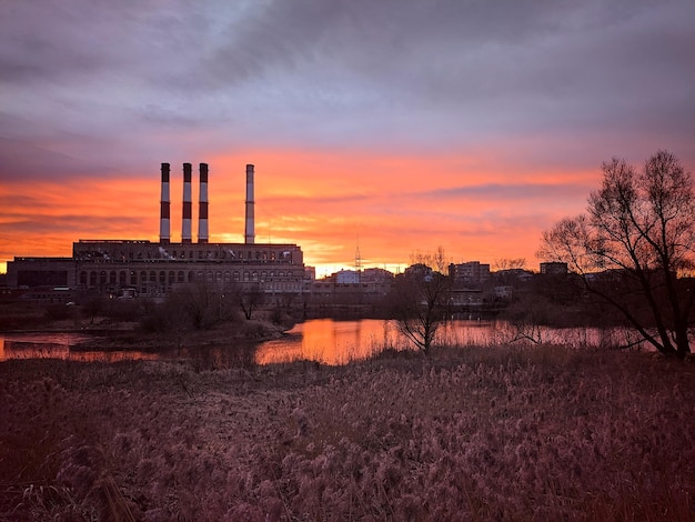 写真 背景の空に沈む美しい夕日パイプのある工場前景には畑があります