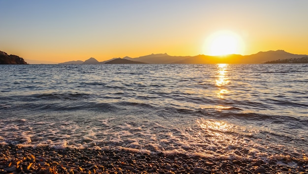 に照らされたビーチに島や山の石がある地中海沿岸の美しい夕日