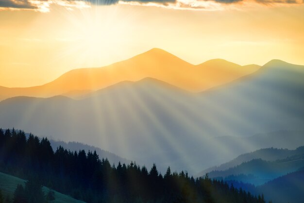 Beautiful sunset in the mountains with sunrays. Landscape with sun shining through orange clouds