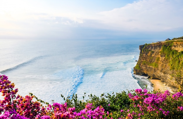 Красивый заход солнца на побережье океана около виска Uluwatu, Бали, Индонезии. Цветы на морских волнах на закате.