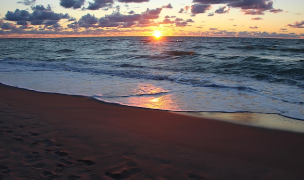 雲と海の泡に赤い反射と海に沈む美しい夕日
