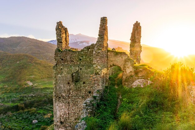 Beautiful sunset or sunrise landscape of ancient ruins on a top of a hill with green mountains with white snow top on background