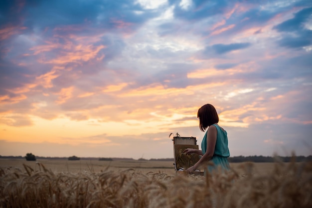 麦畑の美しい夕日、明るくカラフルな雲、穏やかなロマンチックな雰囲気。暖かい夏の夜に彼女の絵を終える女性アーティストの女の子。