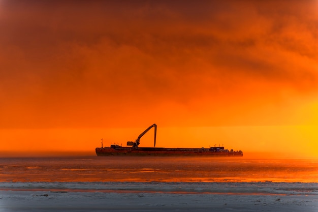 Photo beautiful sunset with fog in arctic sea. barge with excavator.