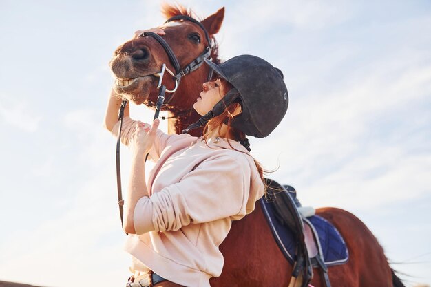 美しい日差し昼間に農業分野で彼女の馬と一緒に立っている若い女性