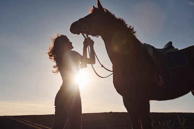 Beautiful sunshine Young woman standing with her horse in agriculture field at daytime