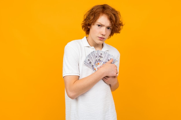Beautiful surprised boy holds a fan of money notes in his hands on a yellow studio wall